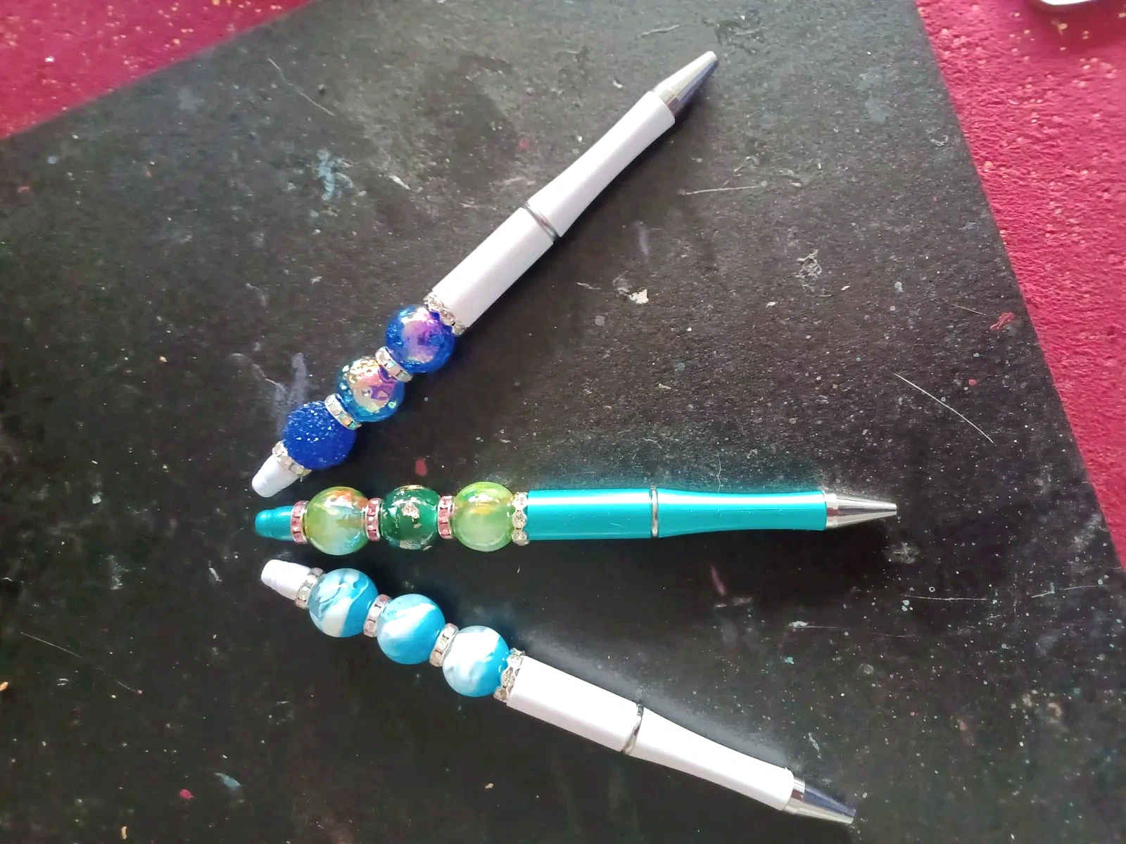Detail van drie kralenpennen in blauw, groen en wit